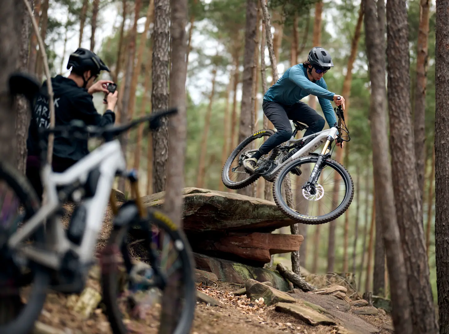 Ein Mountainbiker fotografiert einen anderen mit seinem Focus Jam2 beim Sprung im Wald